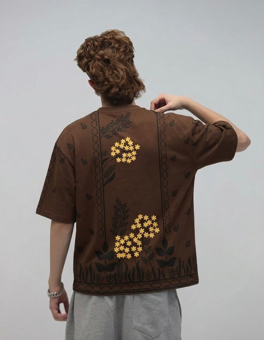 Person wearing a brown t-shirt with floral patterns on a plain background