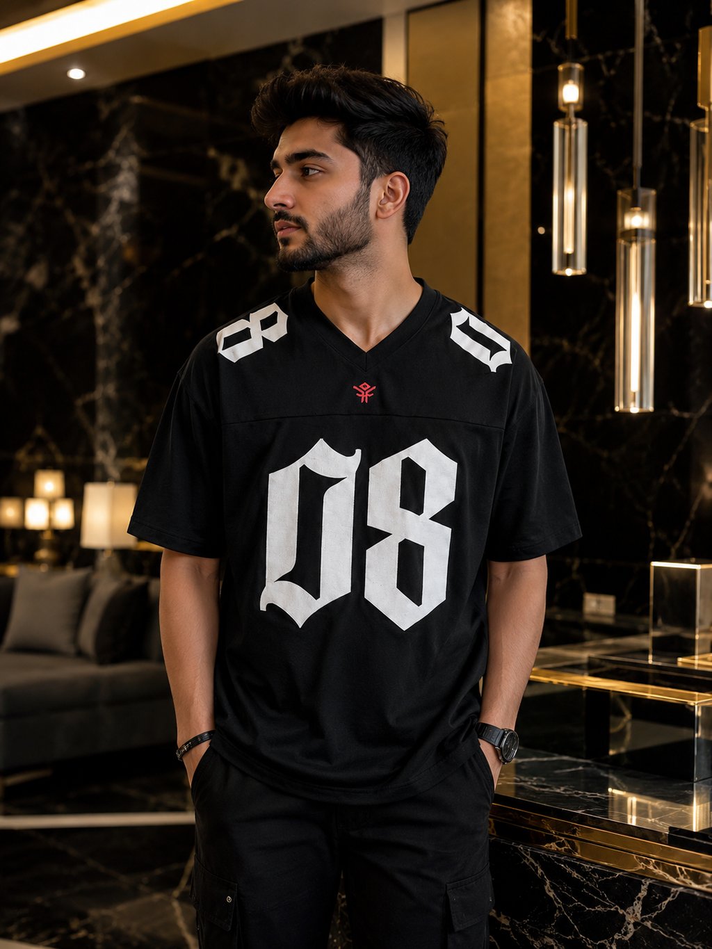 A man wearing a black V-neck jersey with a large white gothic-style '08' on the front, standing in a luxury black marble lobby.