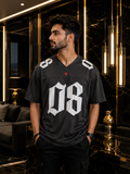 A man wearing a black V-neck football jersey with large white '08' lettering on the front, standing in a luxurious modern room with black marble and gold accents.