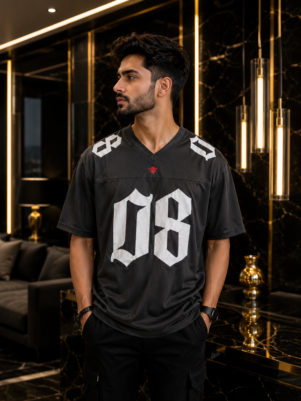 A man wearing a black V-neck football jersey with large white '08' lettering on the front, standing in a luxurious modern room with black marble and gold accents.
