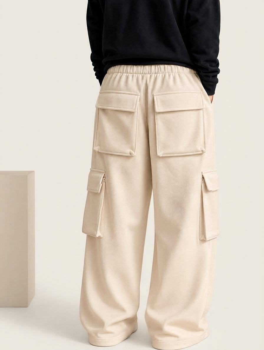 A person shown from the back wearing wide-leg cream cargo pants with large flap pockets and a black sweatshirt, photographed in a clean studio setting.