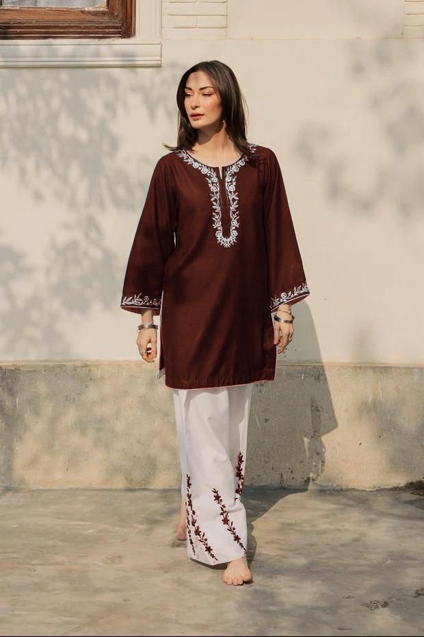 Woman wearing a brown embroidered top and white pants standing outdoors.