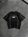 A black short-sleeve t-shirt with white contrast piping and a white graphic logo on the chest, laid flat on a dark gray tiled floor.