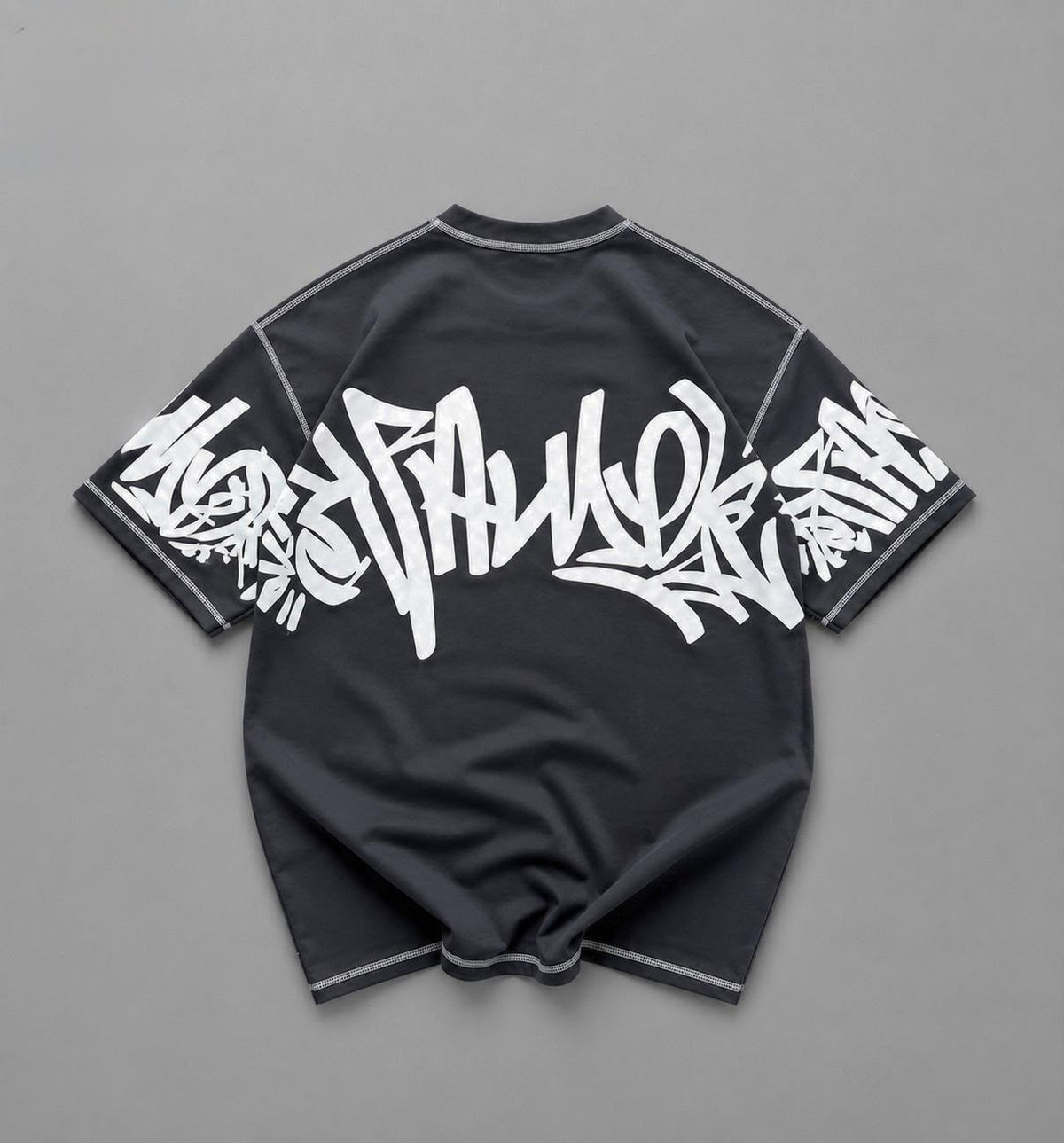 A black short-sleeve t-shirt with a large white graffiti-style graphic across the back and white piping details, laid flat on a gray background.