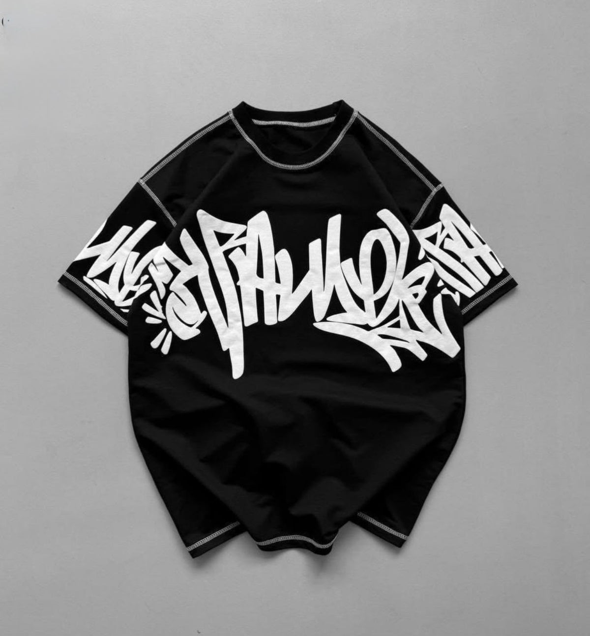 A black short-sleeve t-shirt with a large white graffiti-style graphic across the chest, laid flat on a neutral gray background.