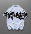A white short-sleeve t-shirt with black graffiti-style lettering across the back and black piping on the shoulders and hem, laid flat on a gray background.