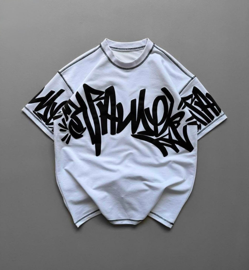 A white short-sleeve t-shirt with a large black graffiti-style graphic across the chest and sleeves, laid flat on a neutral gray background.