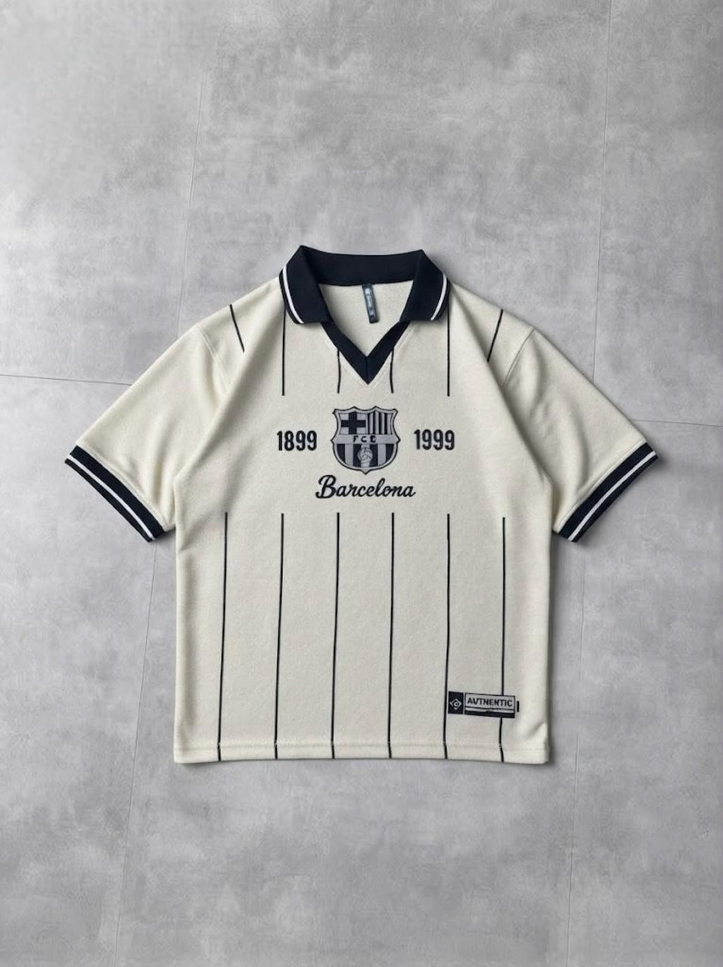 A vintage-style FC Barcelona short-sleeve polo shirt in off-white with navy blue pinstripes and trim, laid flat on a textured gray background.