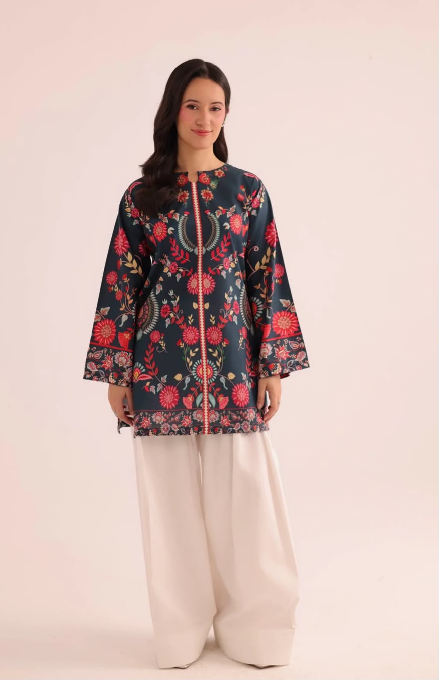 A woman modeling a dark navy blue kurta with a vibrant red, pink, and green floral print, paired with wide-leg cream trousers, against a solid pale pink studio background.
