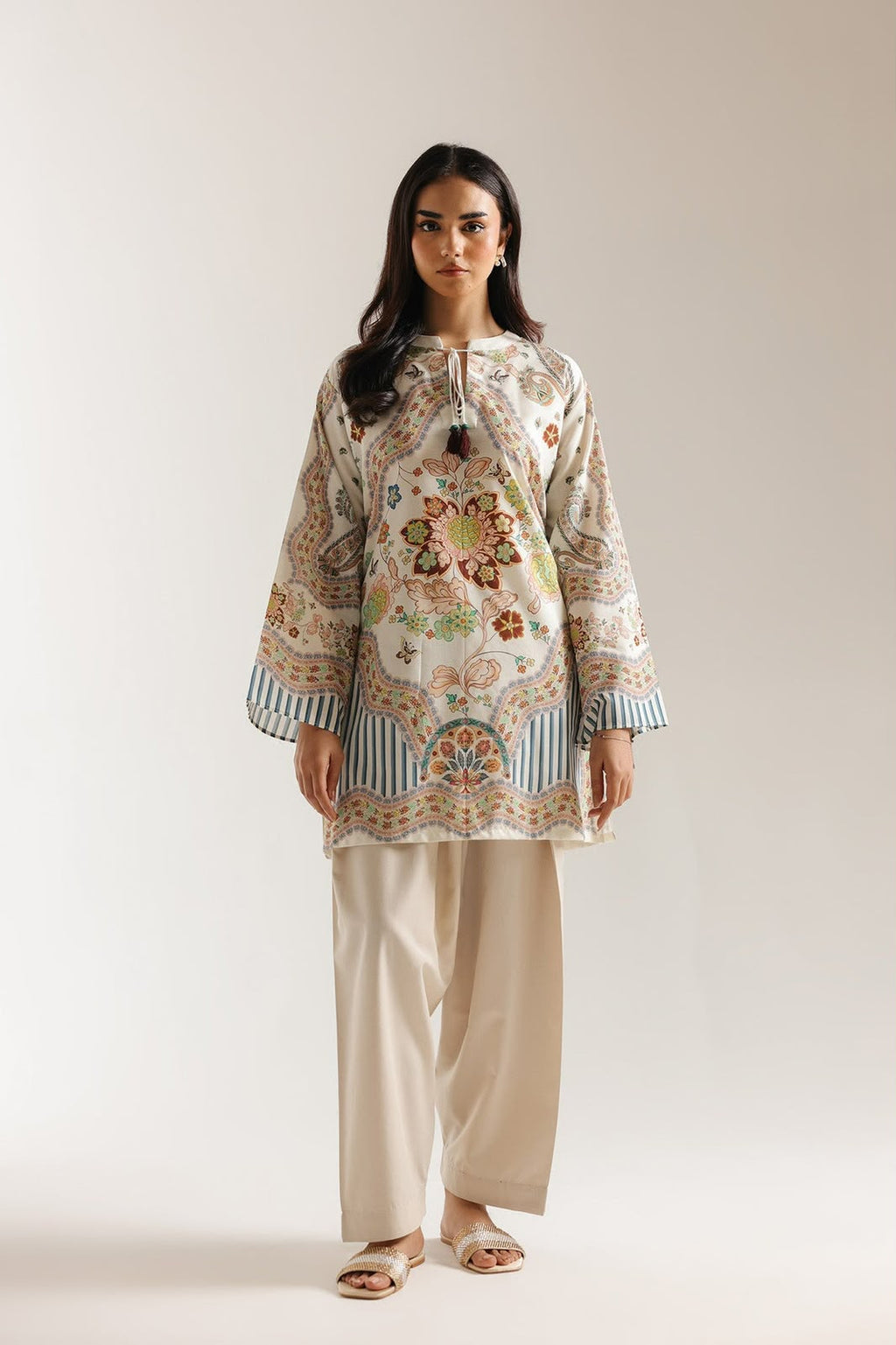 Woman wearing a floral patterned top and beige pants on a plain background