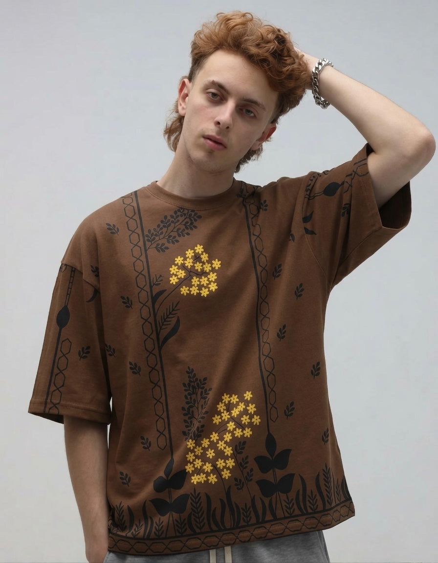 Person wearing a brown t-shirt with floral patterns on a plain background
